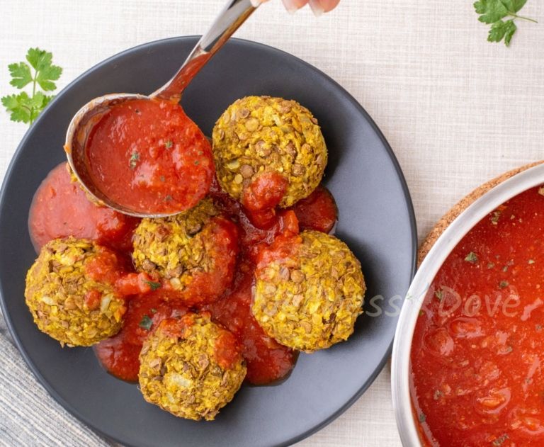 vegan meatballs in a plate, a ladle pouring tomato sauce over, overhead view