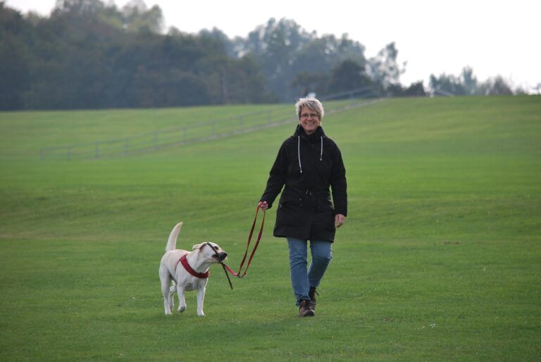 A woman walking her dog in a field.