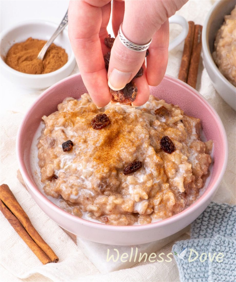 the  quick vegan brown rice pudding in a bowl and a hand is sprinkling some raisins on it
