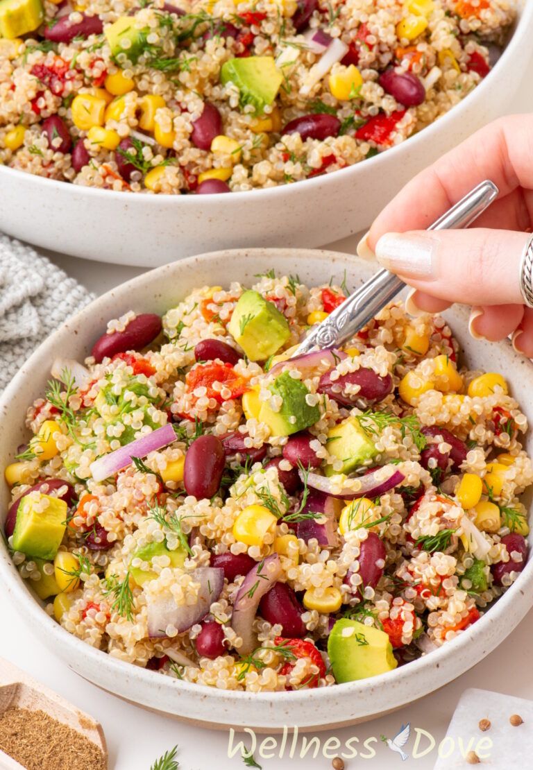 the vegan avocado quinoa salad in a bowl - a hand is stirring it with a spoon