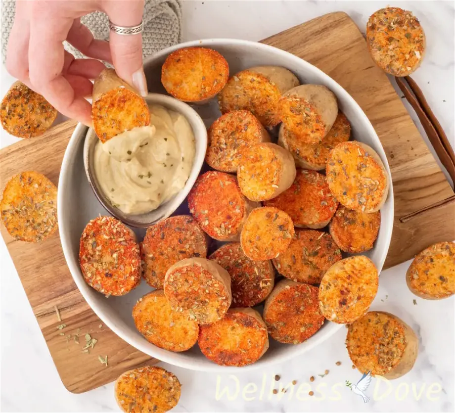 the the vegan oven baked potatoes with herbs in a bowl - overhead view - a hand is dipping a potato in some hummus 