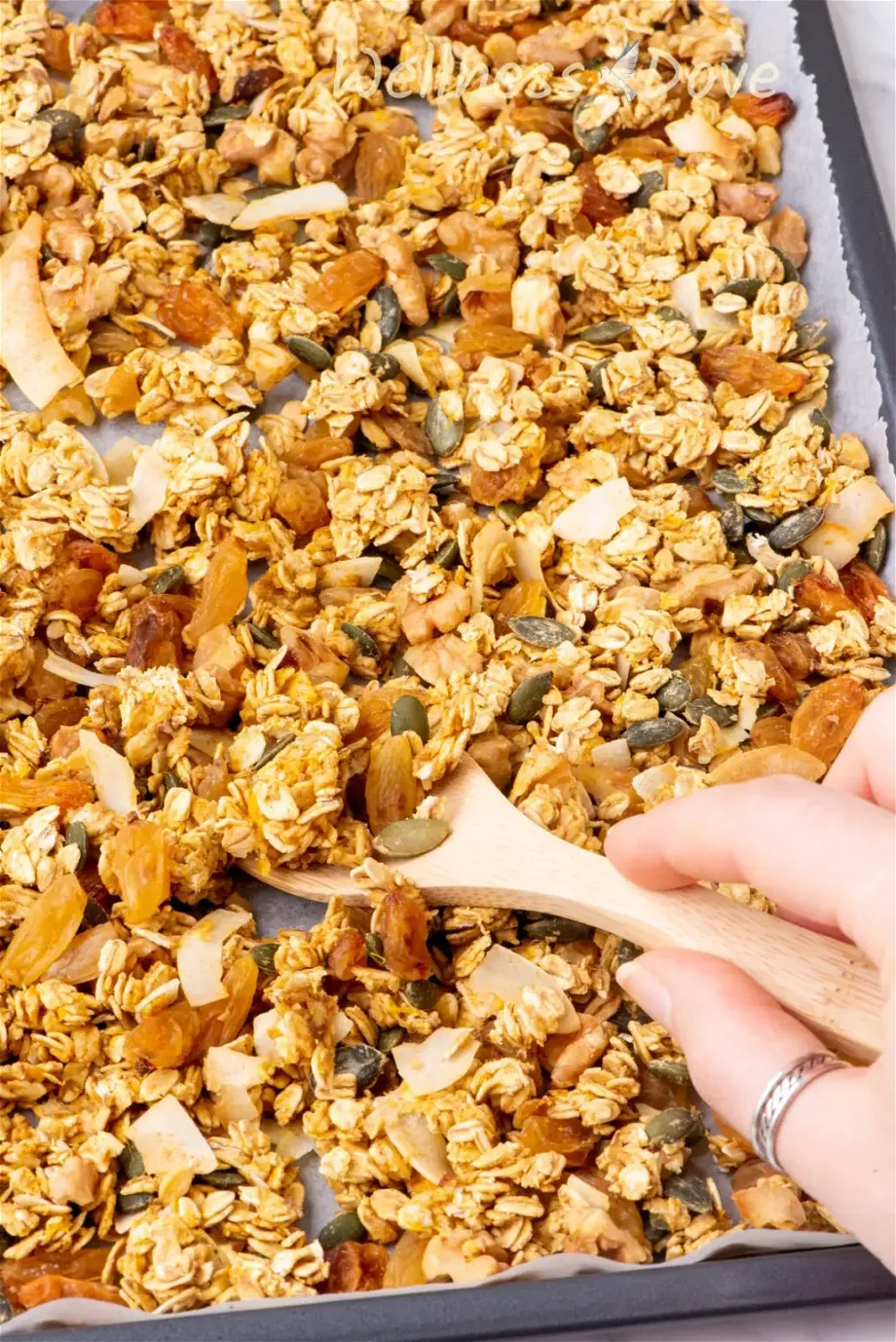 a macro shot of the homemade vegan sugar-free granola recipe  while a hand is taking some out with a wooden spoon