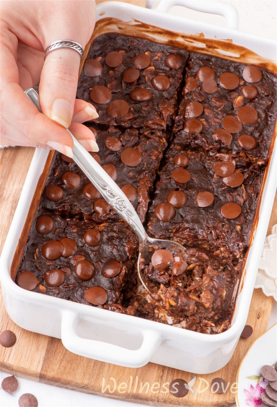 a 3/4 view of the Vegan Brownie Baked Oatmeal, a piece is missing and a hand is taking some of the brownie away with a spoon
