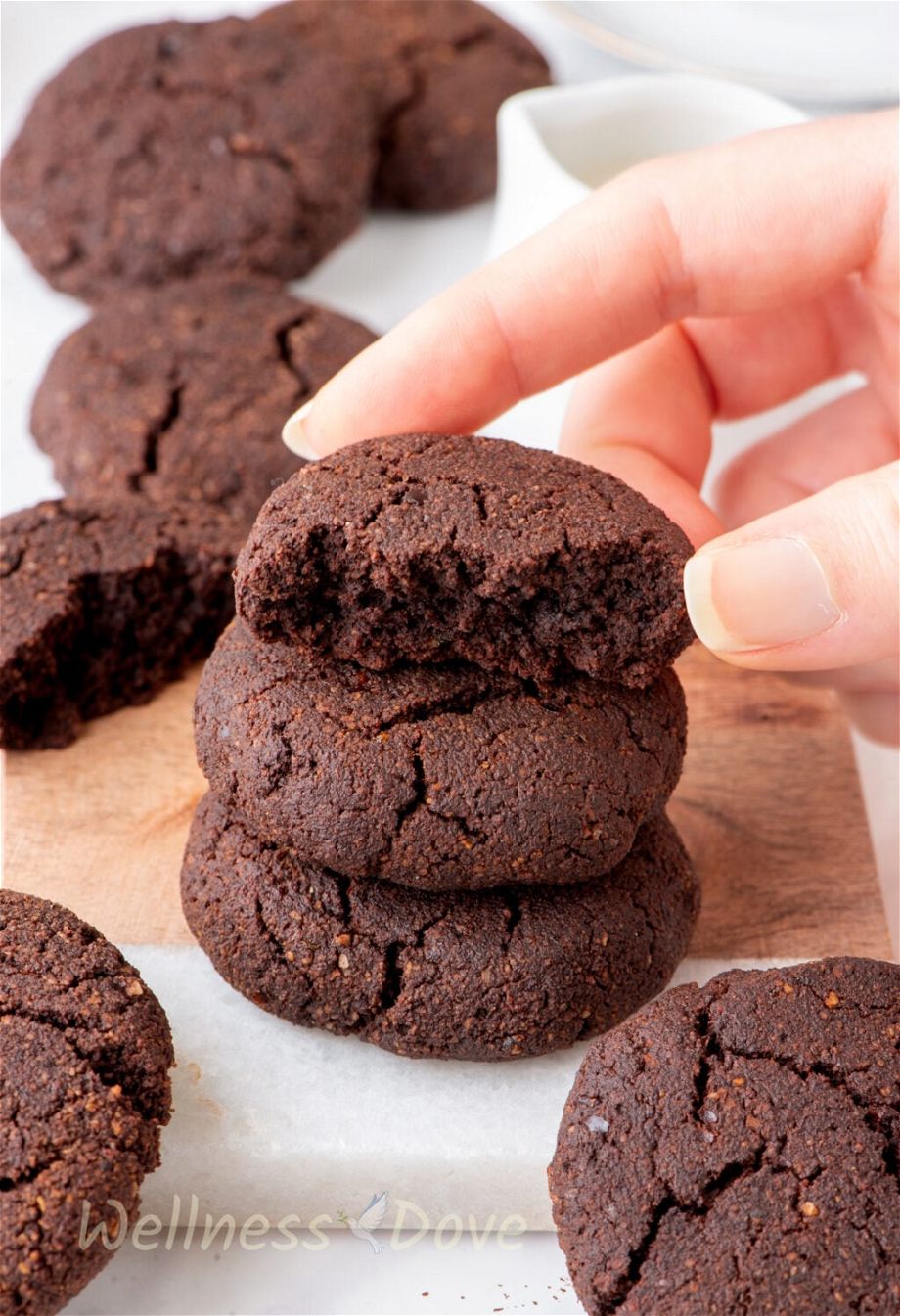 the Easy Chocolate Almond Vegan Cookies on a small chopping board and a hand is holding one of them