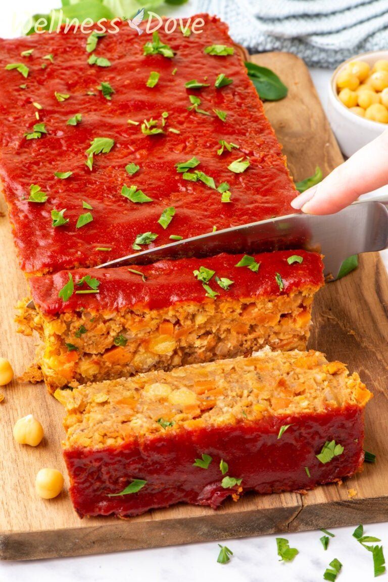 the vegan chickpea meatloaf on a chopping board while a knife is cutting it into pieces