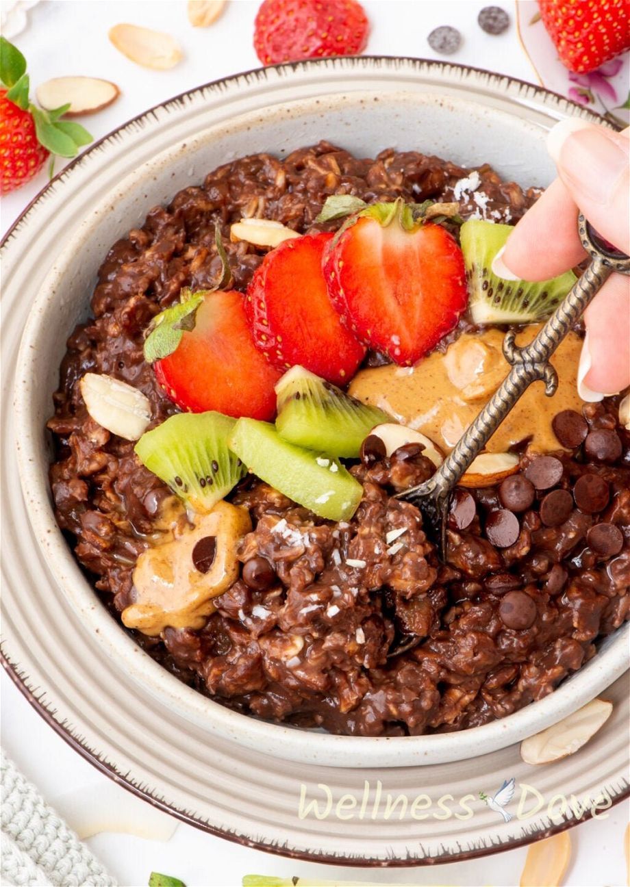 the  chocolate vegan oatmeal in a bowl and a hand is taking some of the  chocolate vegan oatmeal with a small spoon