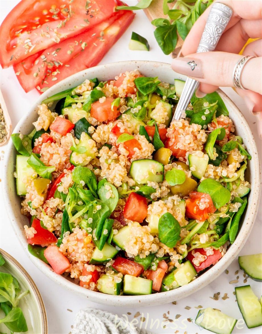the easy quinoa vegan summer salad in a smaller bowl and a hand is taking some out with a spoon