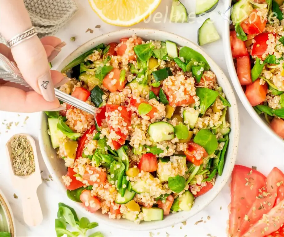 an overhead shot of the easy quinoa vegan summer salad in a smaller bowl while a person is taking out some of it with a spoon