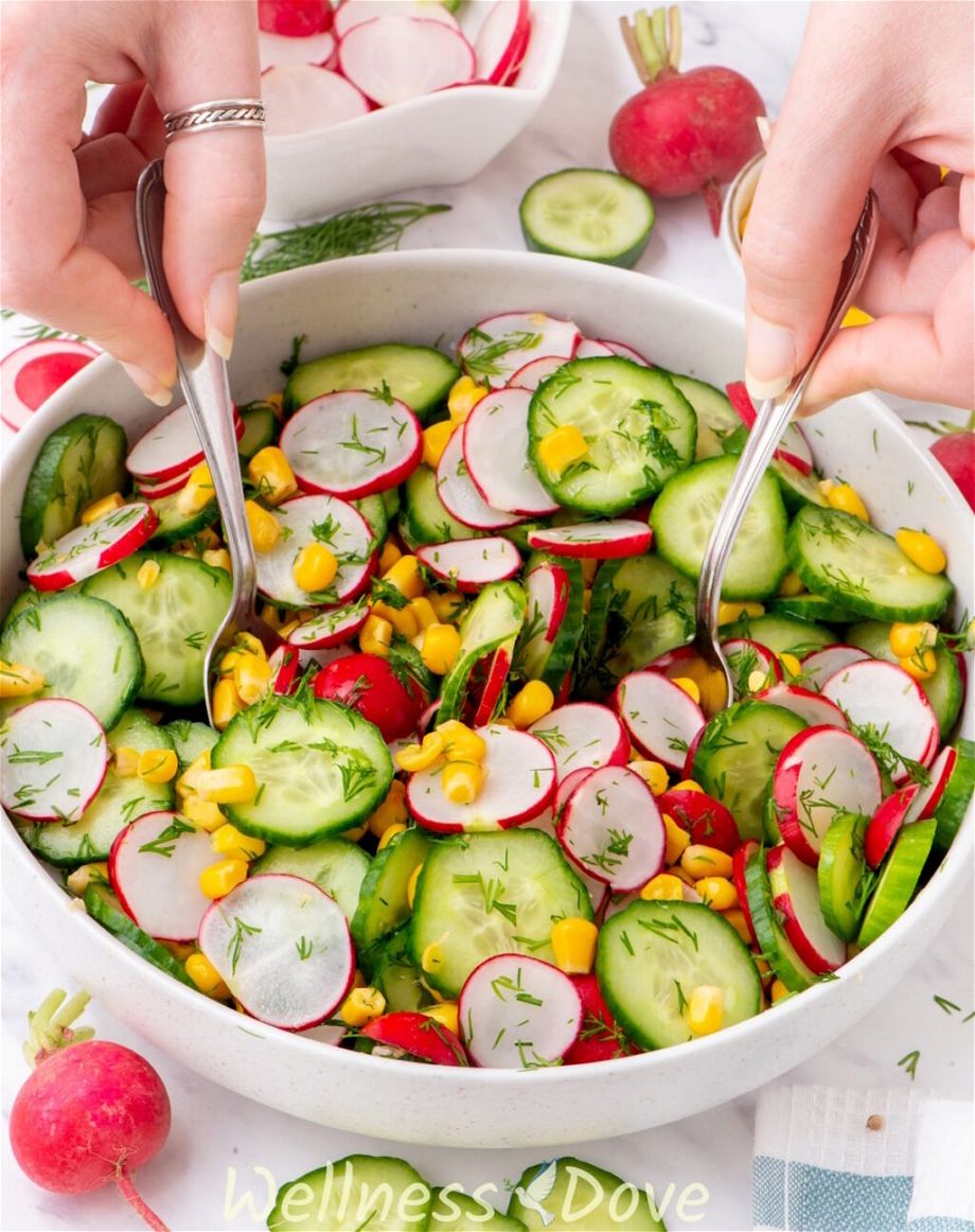 the Fresh Cucumber Summer Vegan Salad in a larger bowl - two hands are tossing it