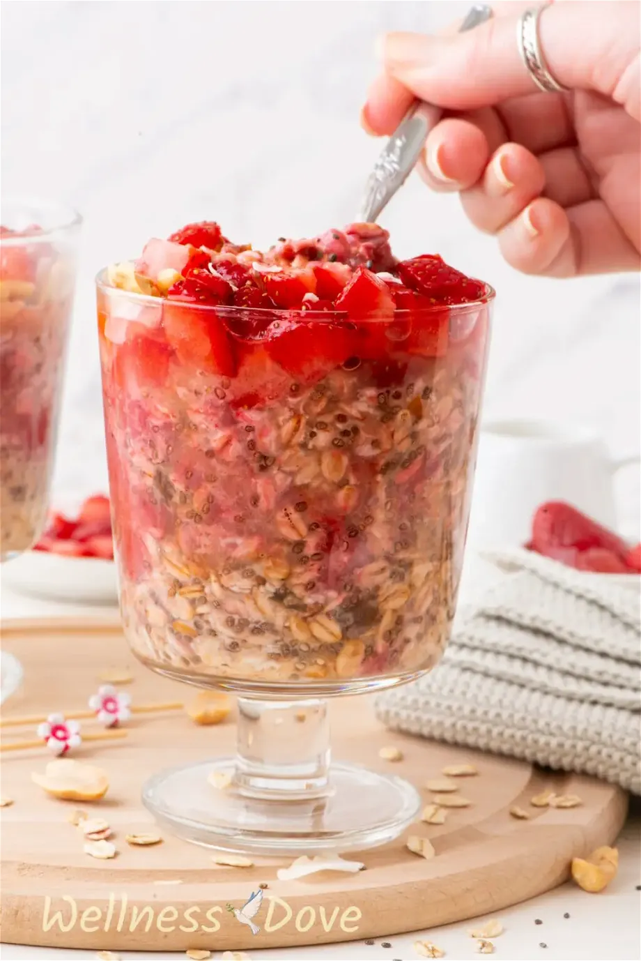 the Easy Overnight Oats with Strawberries, a front view while a hand is taking some of the oats with a spoon 