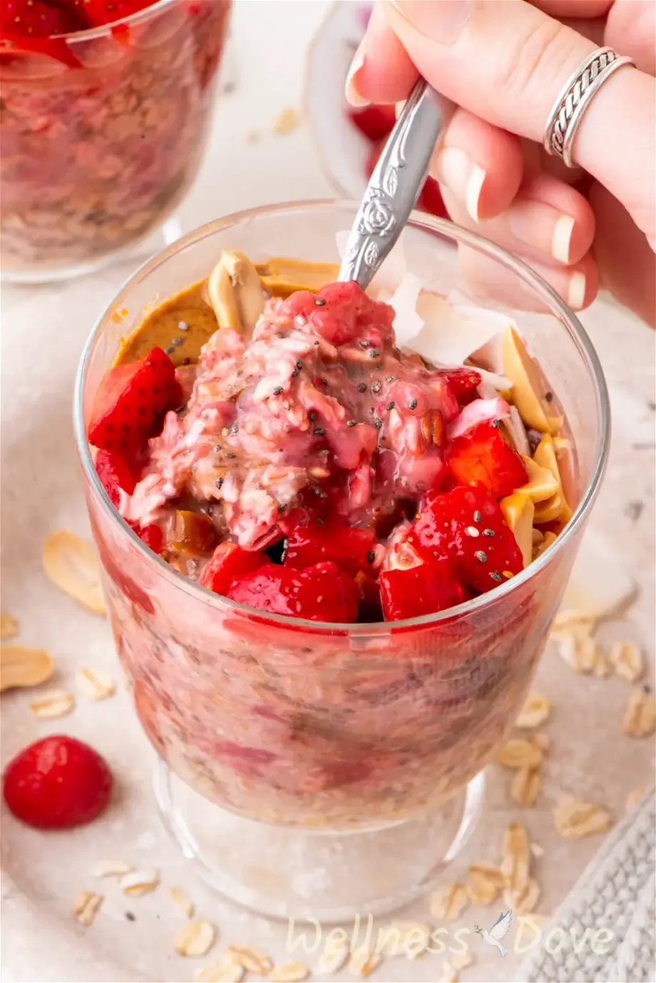 the Easy Overnight Oats with Strawberries in a glass, a person is taking some of them with a spoon