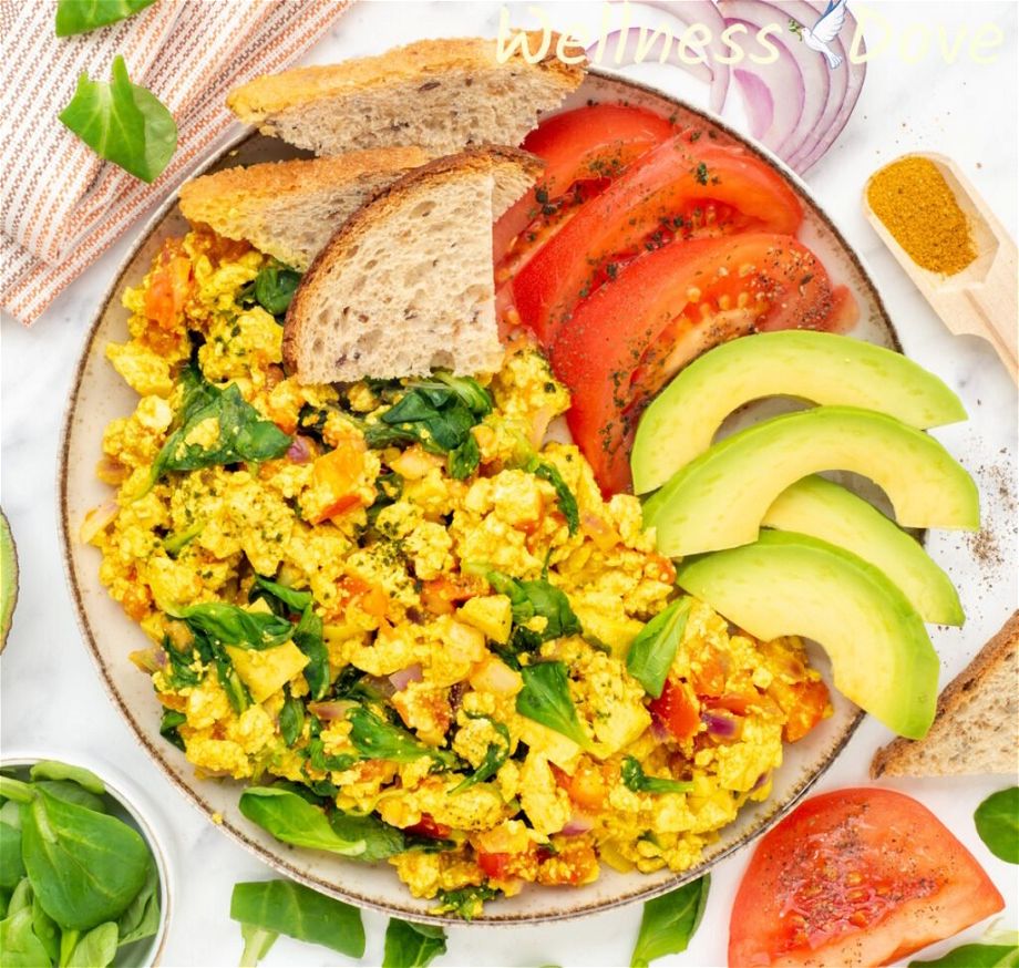 an overhead photo of the quick curried tofu vegan egg scramble in a plate with tomatoes and avocado