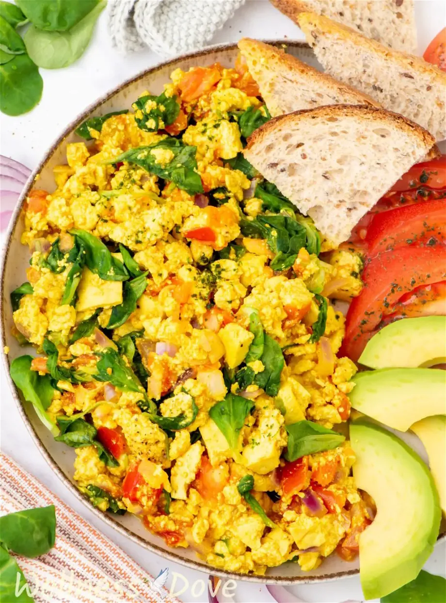 a 3/4 photo of the quick curried tofu vegan egg scramble in a plate with bread, avocado and tomatoes
