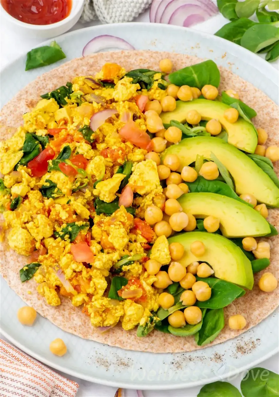 a 3/4 angled photo of the quick curried tofu vegan egg scramble in a plate, on top of a whole wheat wrap