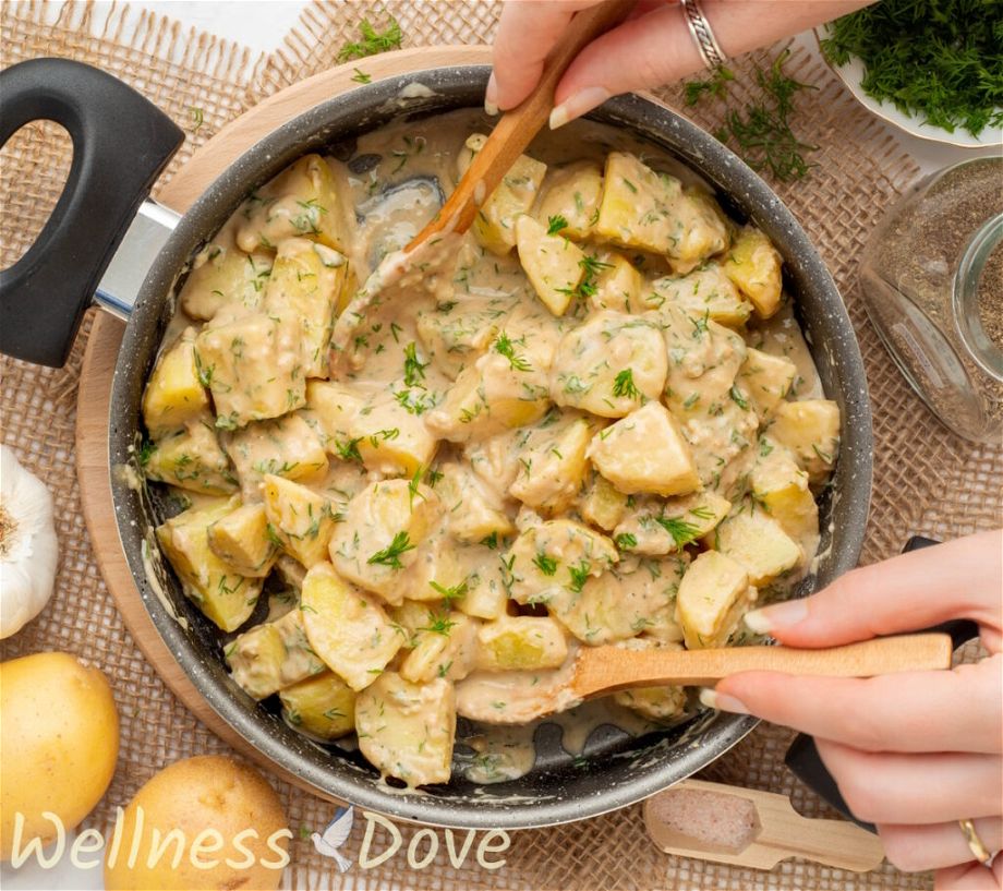 an overhead photo of the Garlic Potatoes in a skillet - two hands are stirring the potatoes