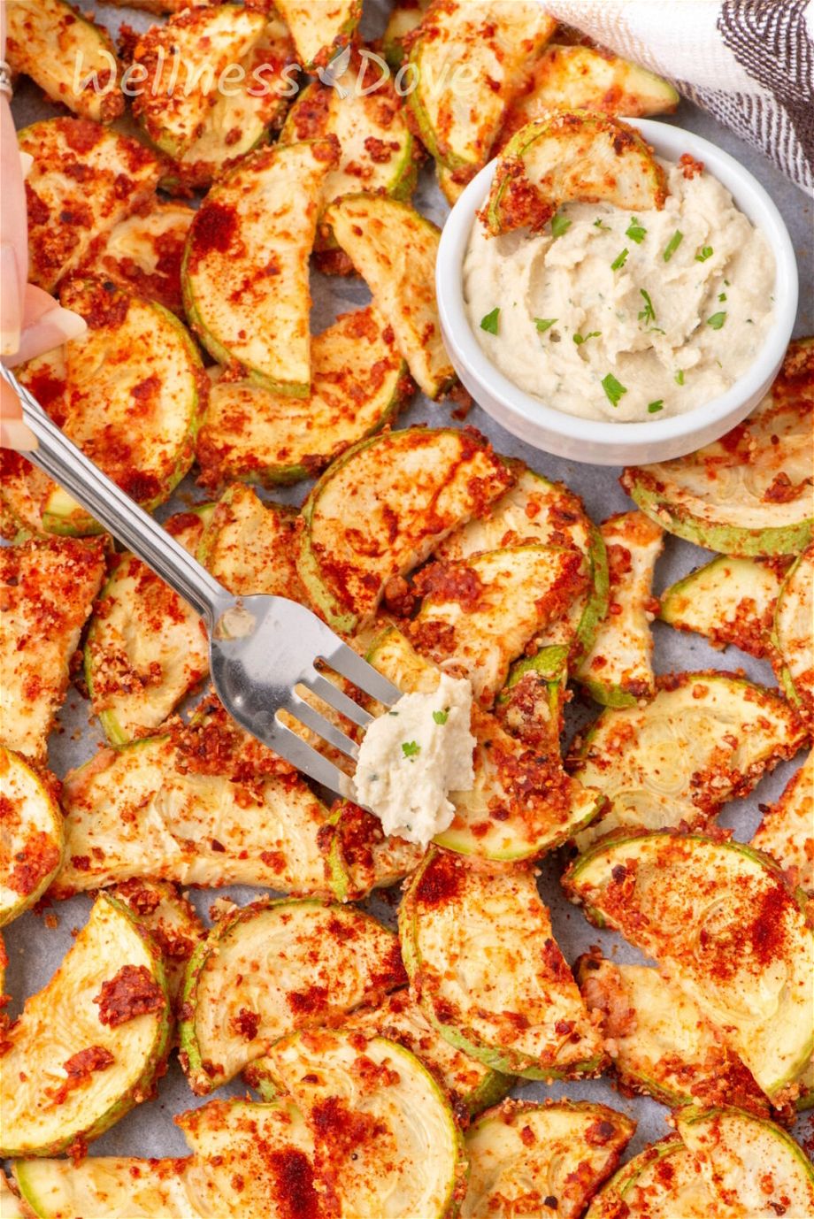 a close up photo of the Easy Oil-free Vegan Baked Zucchini in a baking tray while a fork is taking a zucchini out