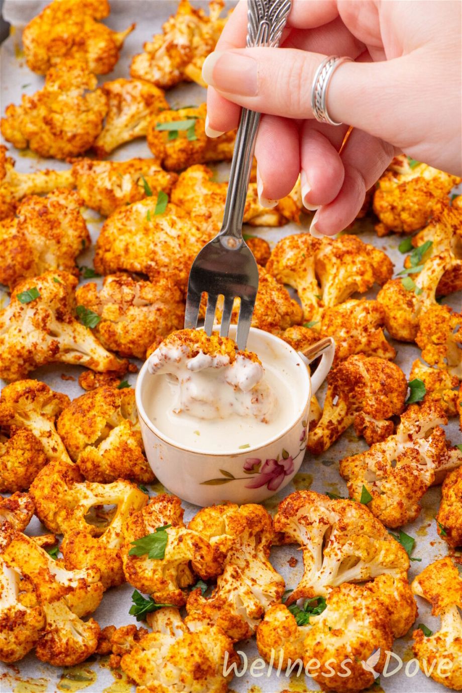 the Oil-free Oven Roasted Cauliflower on a baking tray and a hand is dipping a cauliflower in a cup of sauce