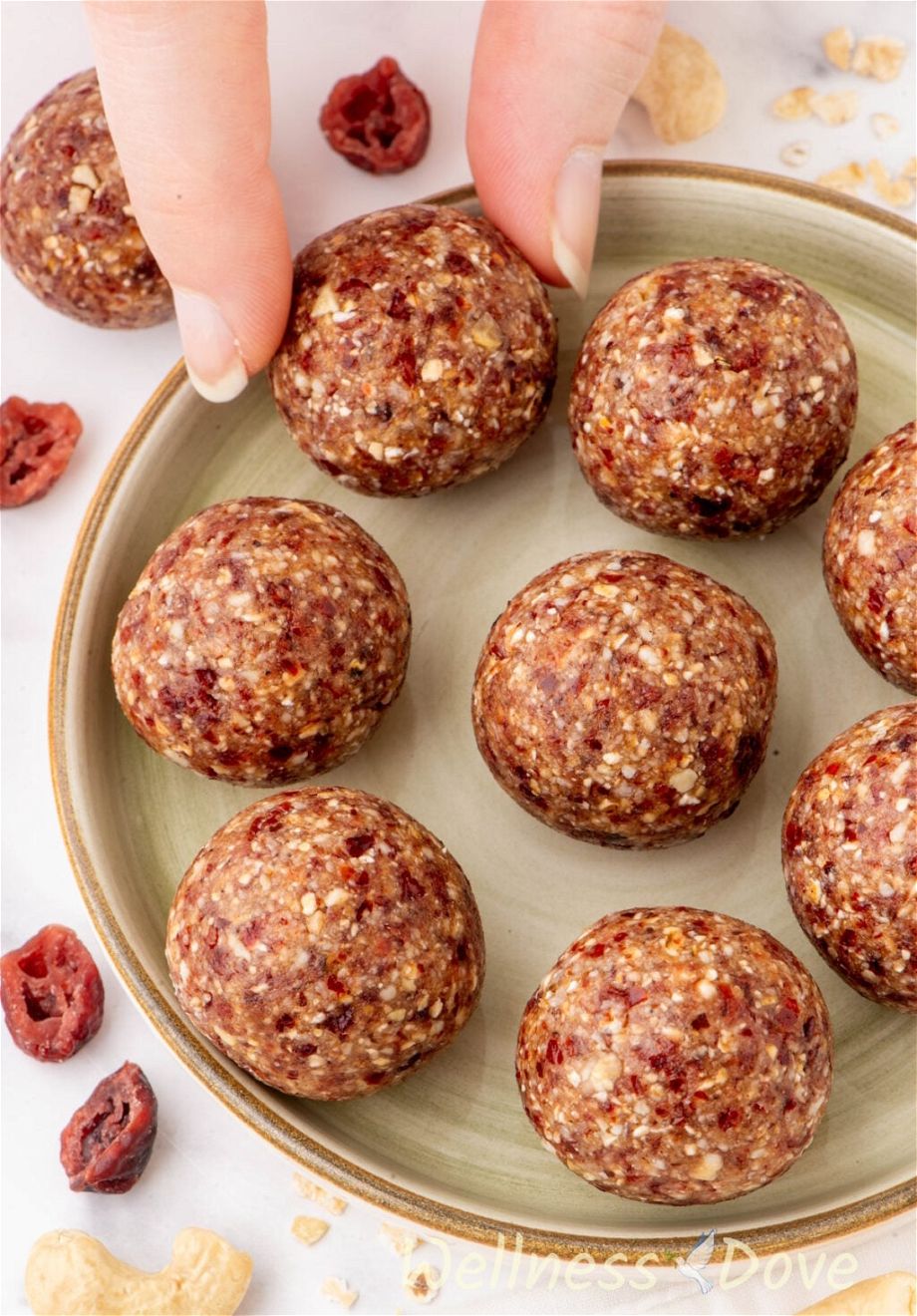 the The Cranberry Oatmeal Vegan Energy Bites in a small plate & a hand is taking one of the balls out
