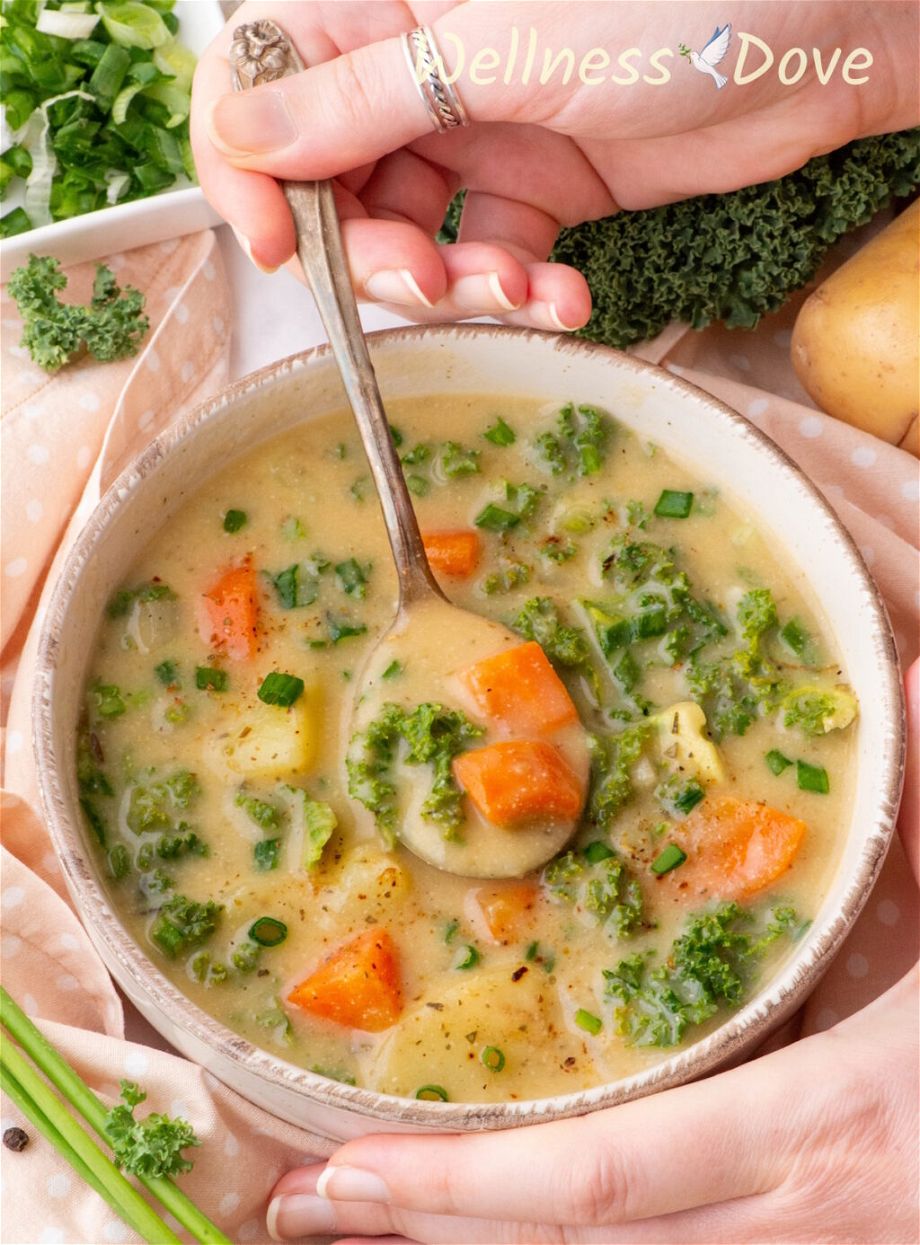 the Creamy Kale Potato Vegan Soup in a bowl and a hand is taking some of it out with a spoon