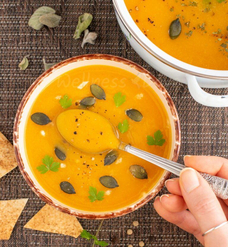 overhead view of a bowl of parsnip soup with a hand holding a spoonful 