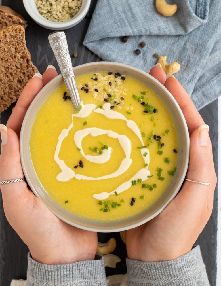 two hands holding a bowl of the zucchini vegan soup