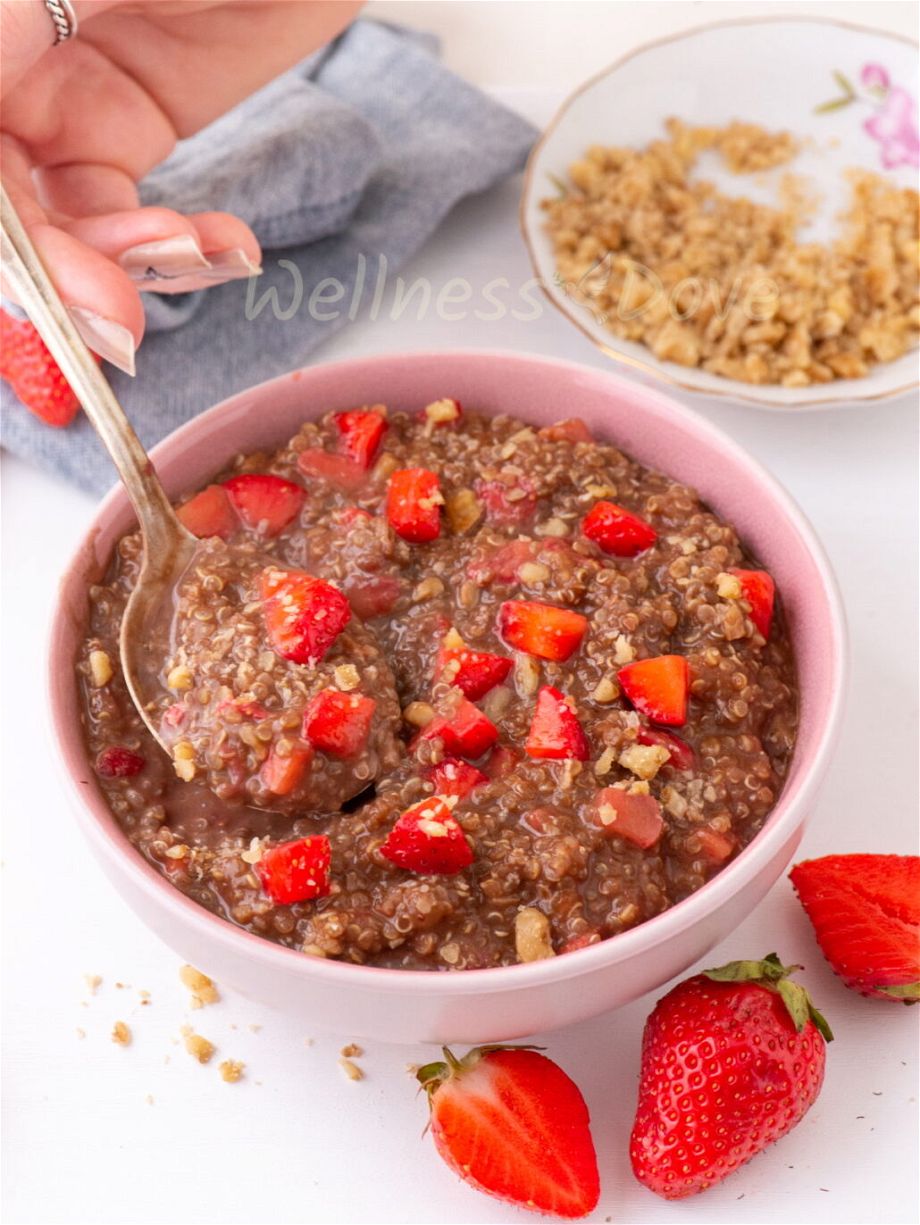 The quinoa vegan breakfast bowl has a spoon in it and a hand is taking a spoonful.