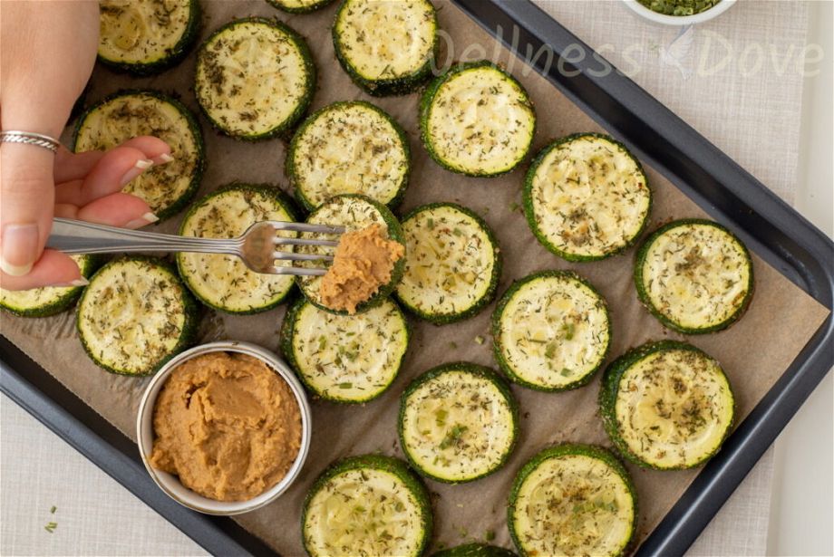 an overhead view of a pan with roasted zucchini and a hand is taking a zucchini with a fork