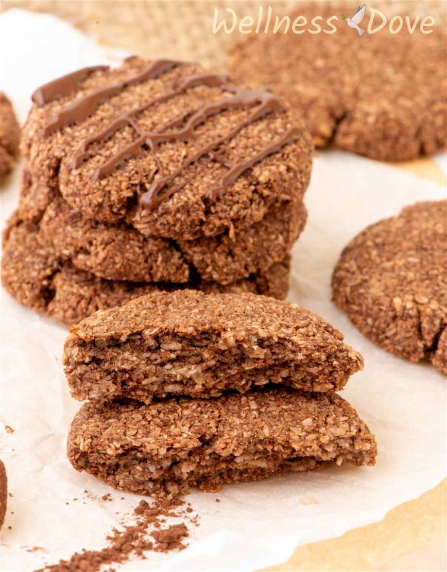 one of the the easy 3 ingredient vegan coconut cookies is broken in half and the two halves are stacked on top of each other. Some other cookies in the beackground