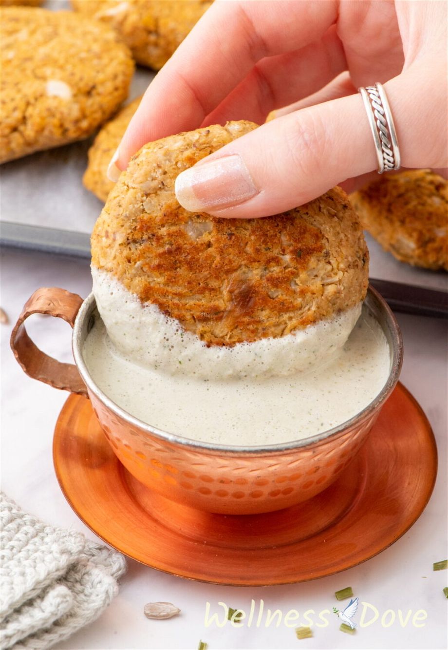 the the easy vegan sunflower seeds sauce  in a copper cup and a hand is taking some of it with a patties