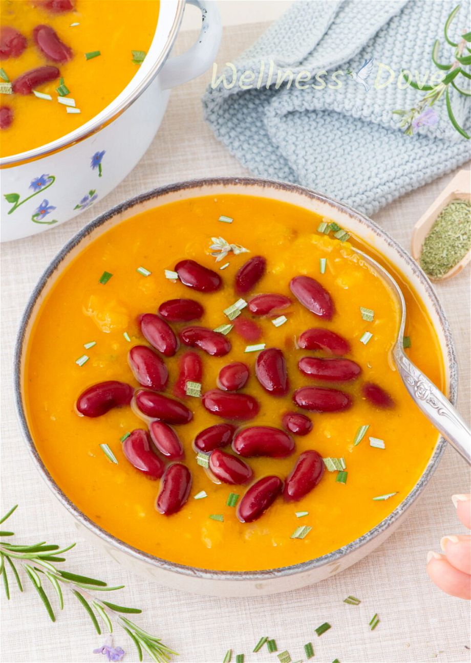 the easy, healthy, and creamy butternut squash vegan soup in a bowl and a hand is taking some aways with a spoon