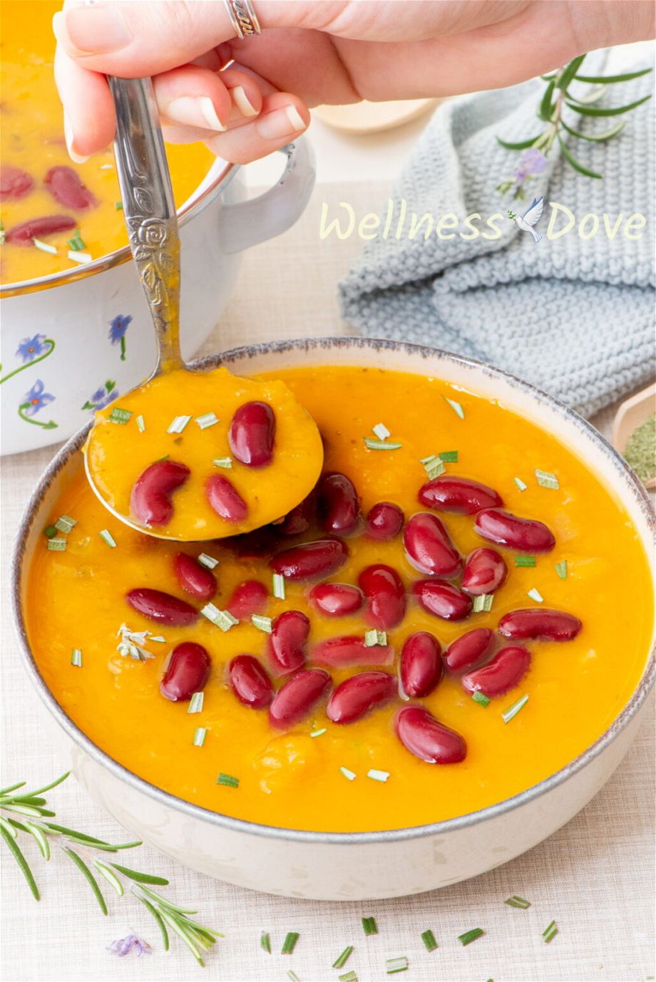 the easy, healthy, and creamy butternut squash vegan soup in a bowl and a hand is taking some aways with a laddle