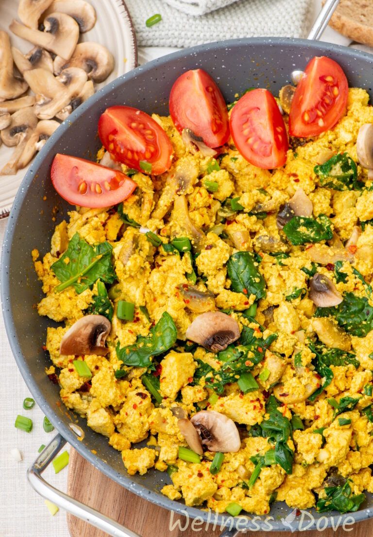 a close up photo of the Vegan Tofu & Spinach Egg Scramble in a pan with some tomatoes in it; 3/4 view