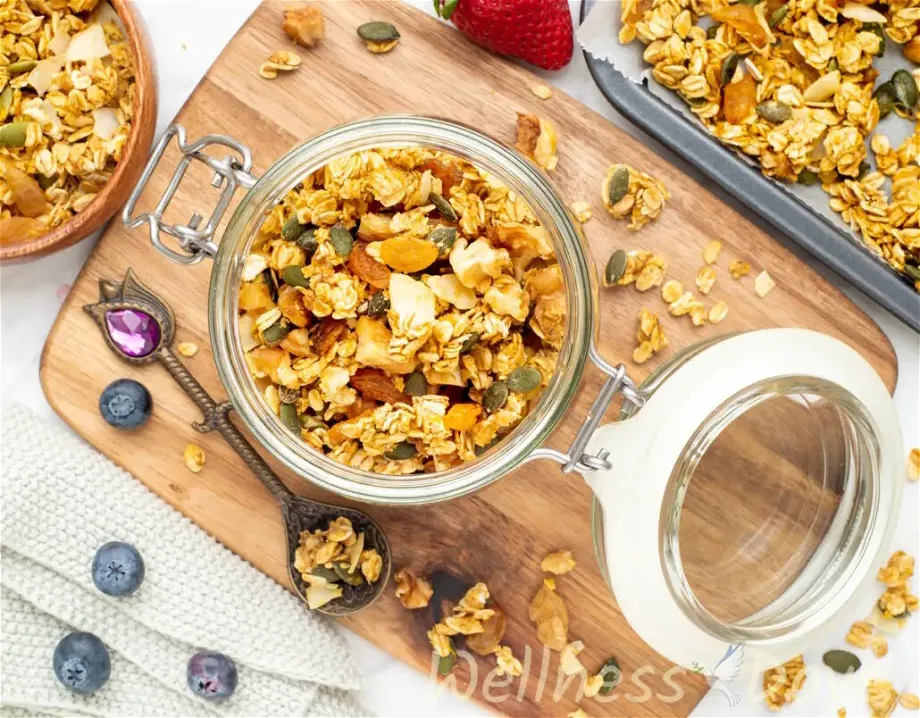 an overhead view of the homemade vegan sugar-free granola recipe in a jar on top a of a wooden chopping board