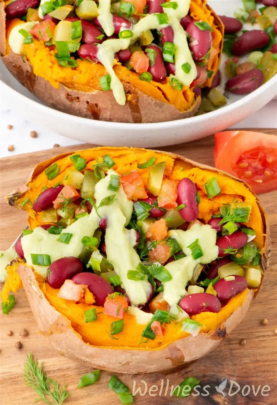 one of the bean stuffed vegan sweet potatoes on top of a chopping board and another in a large bowl