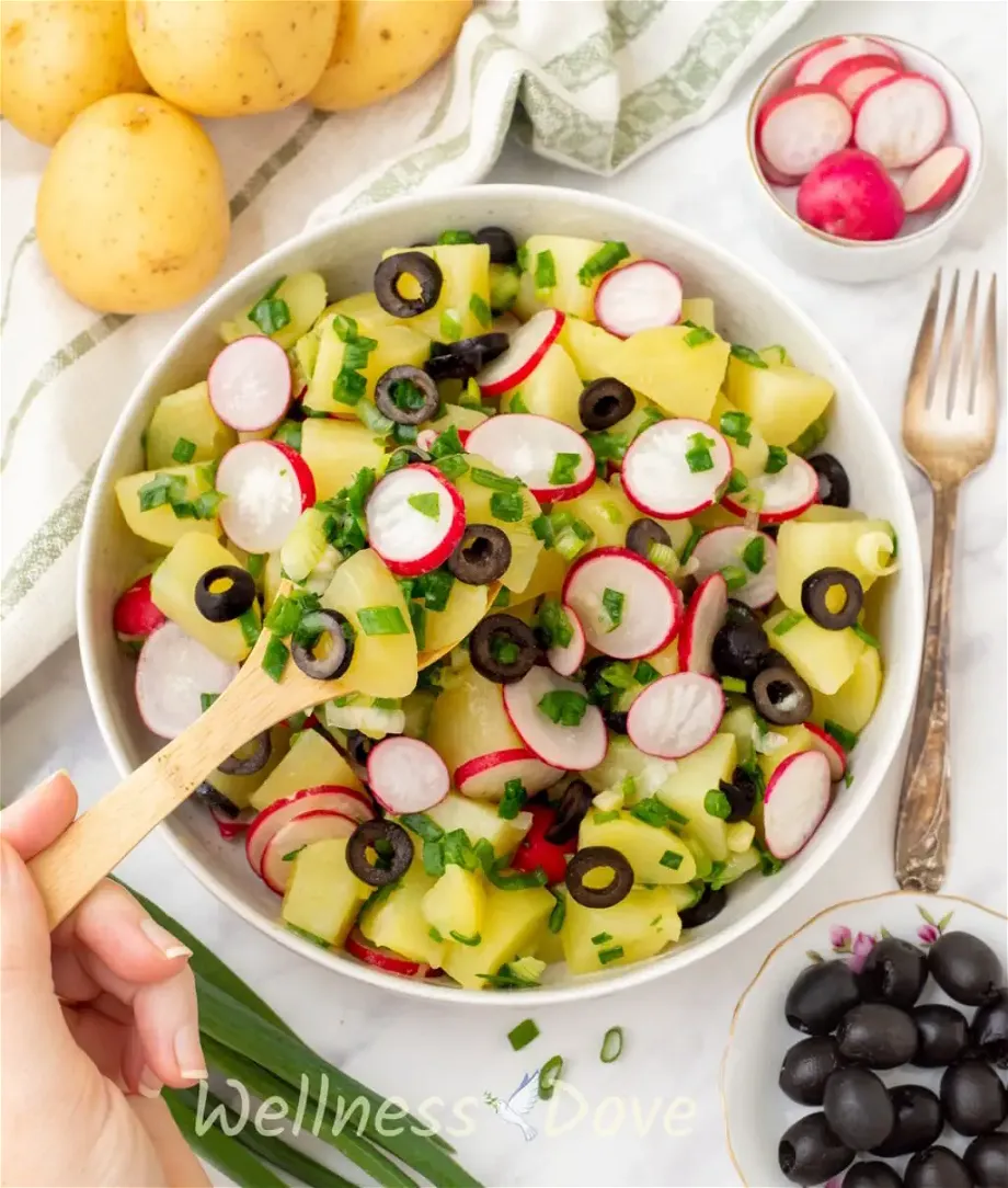 overhead view of the vegan no mayo potato salad - a hand is taking some out with a wooden spoon