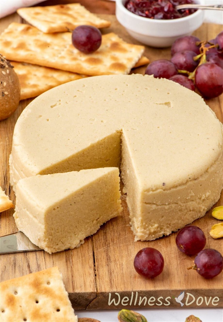 The Vegan Cashew Cheese on a board  while a piece is being taken out