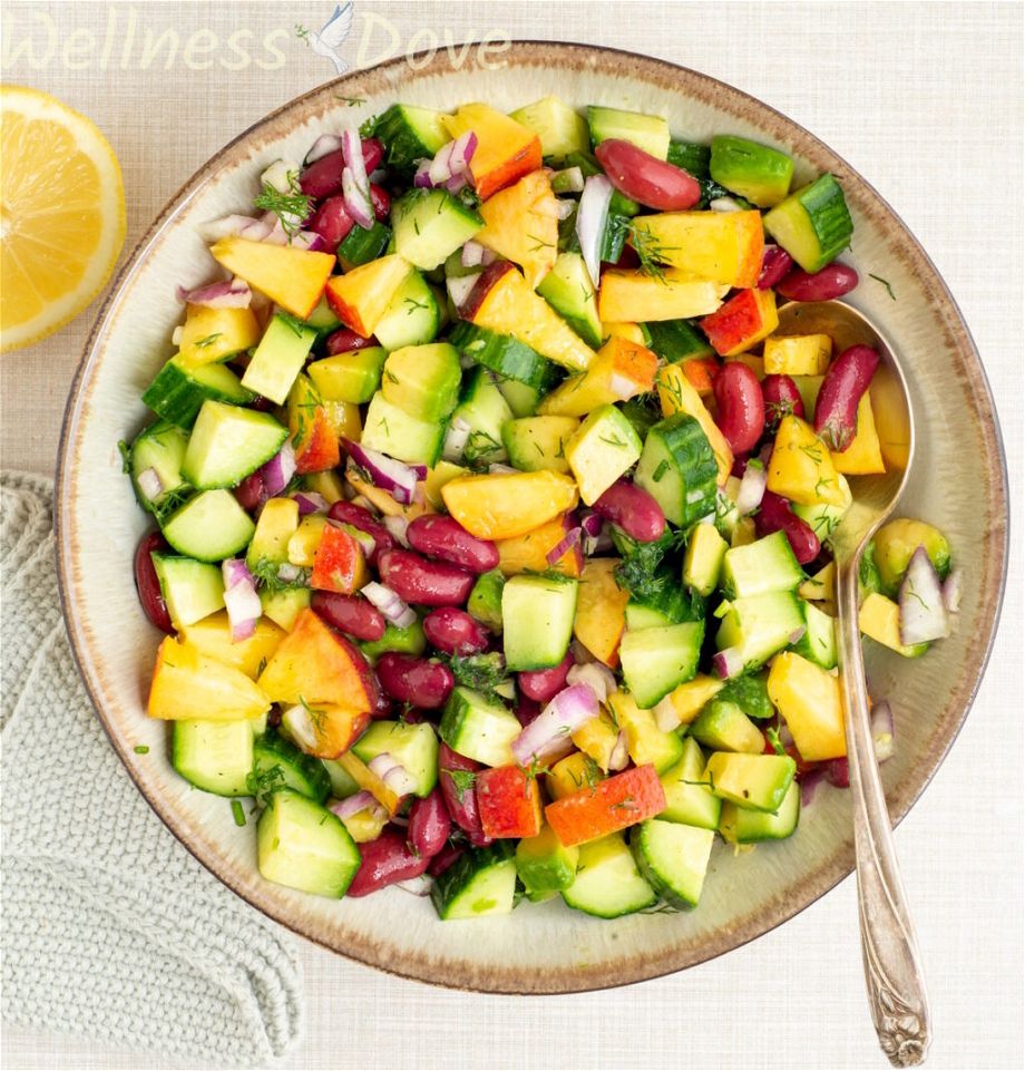 an overhead view of the vegan peach salad with beans in a larger bowl with a spoon inside