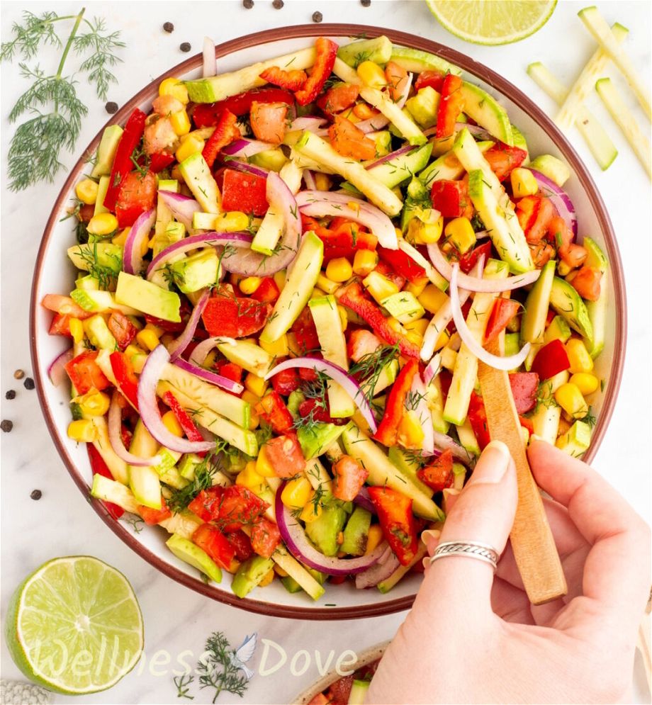 overhead shot of the Refreshing Zucchini Vegan Salad in a bowl while a hand is stirring it with a wooden spoon