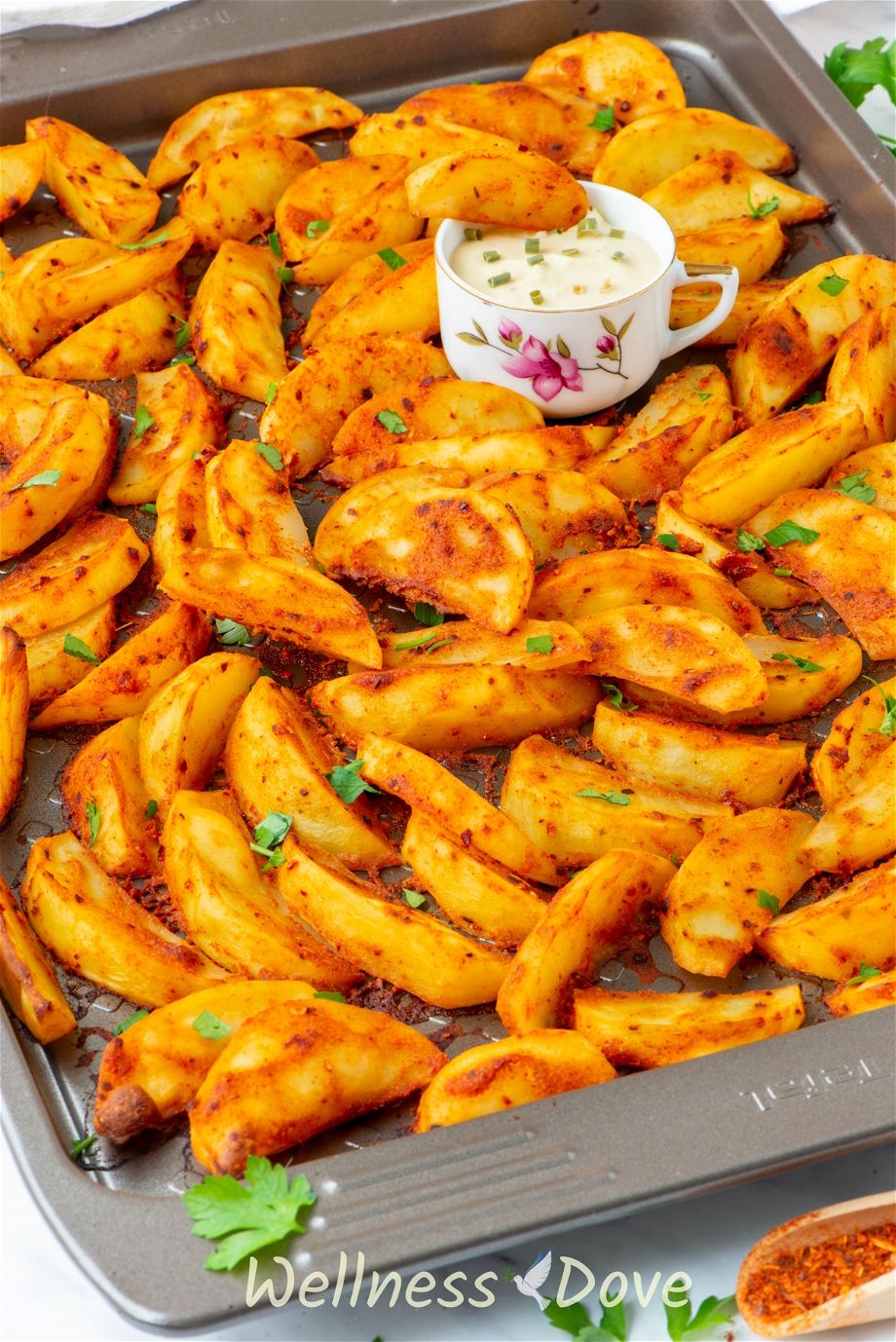 the Baked Mustard Potato Vegan Wedges in a tray, a cup of sauce is in the tray as well