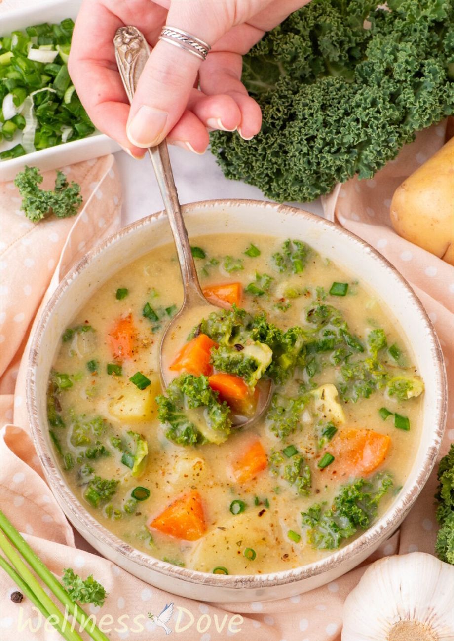 The Creamy Kale Potato Vegan Soup in a small bowl while a hand is taking some of the soup out with a spoon