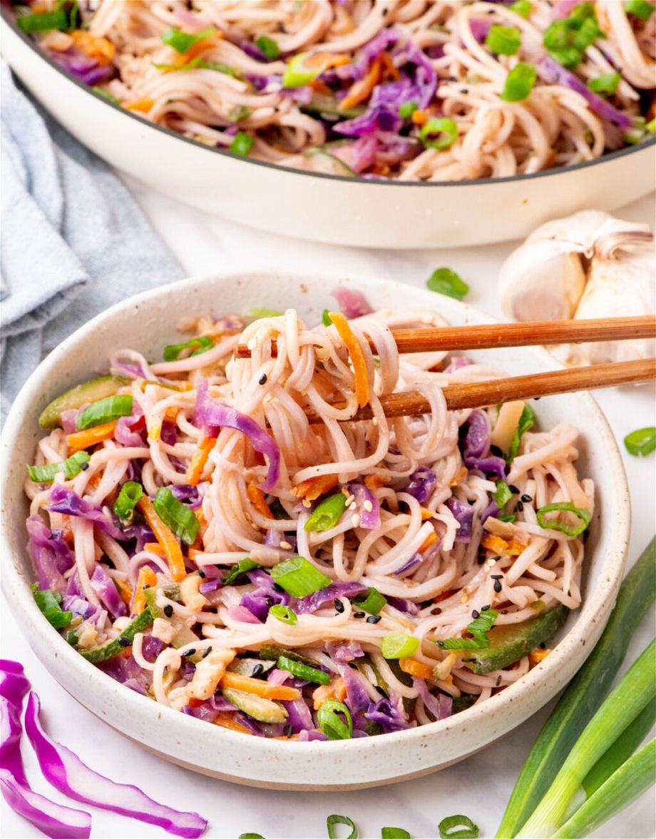 the Quick and Easy Vegan Stir Fry Noodlesin a plate while a hand is taking some out with sticks